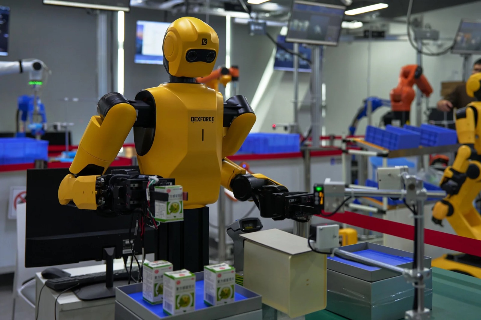 Yellow DexForce humanoid with grippers handling cartons at a demonstration line