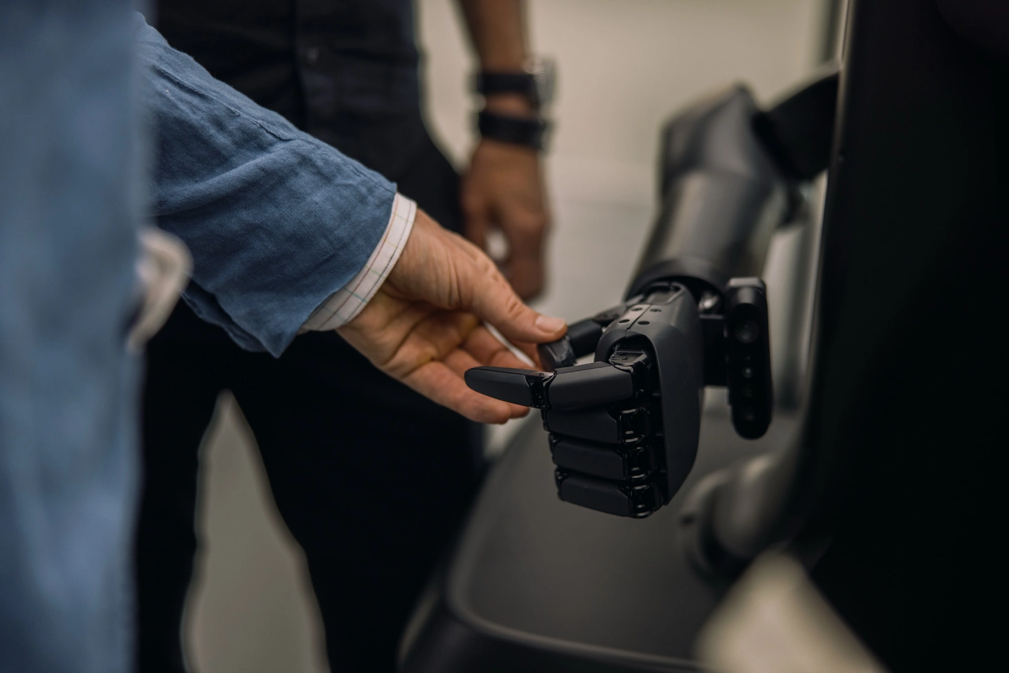 A visitor's hand beside the articulated fingers of a robot gripper